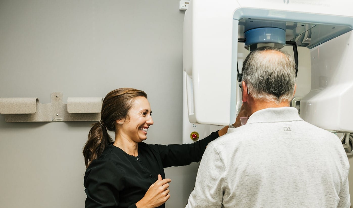 Three female dental professionals in black scrubs smiling and talking inside a dental exam room