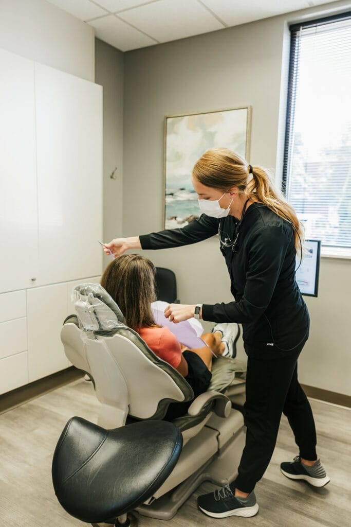 Female dentist in a mask treating a seated female patient in a dental room