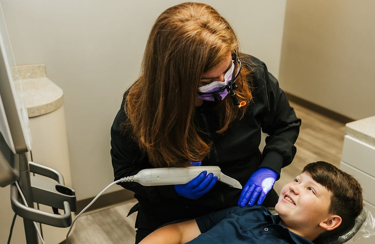 A female dentist using an intraoral scanner while a young boy smiles in the dental chair