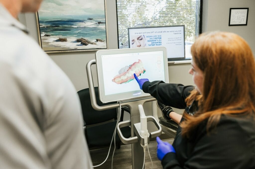 A dentist wearing gloves pointing at a detailed 3D model of teeth on a digital screen