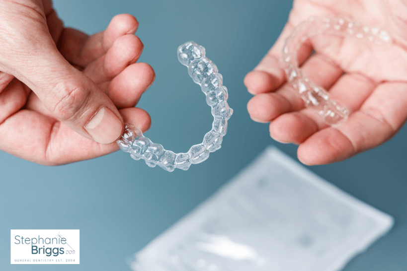 Clear Invisalign aligners being held in hands.